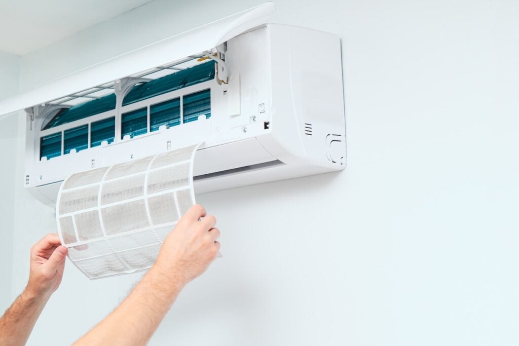 Air conditioner service indoors. Male Technician removing air filter of the air conditioner for cleaning. Air conditioner service and maintenance