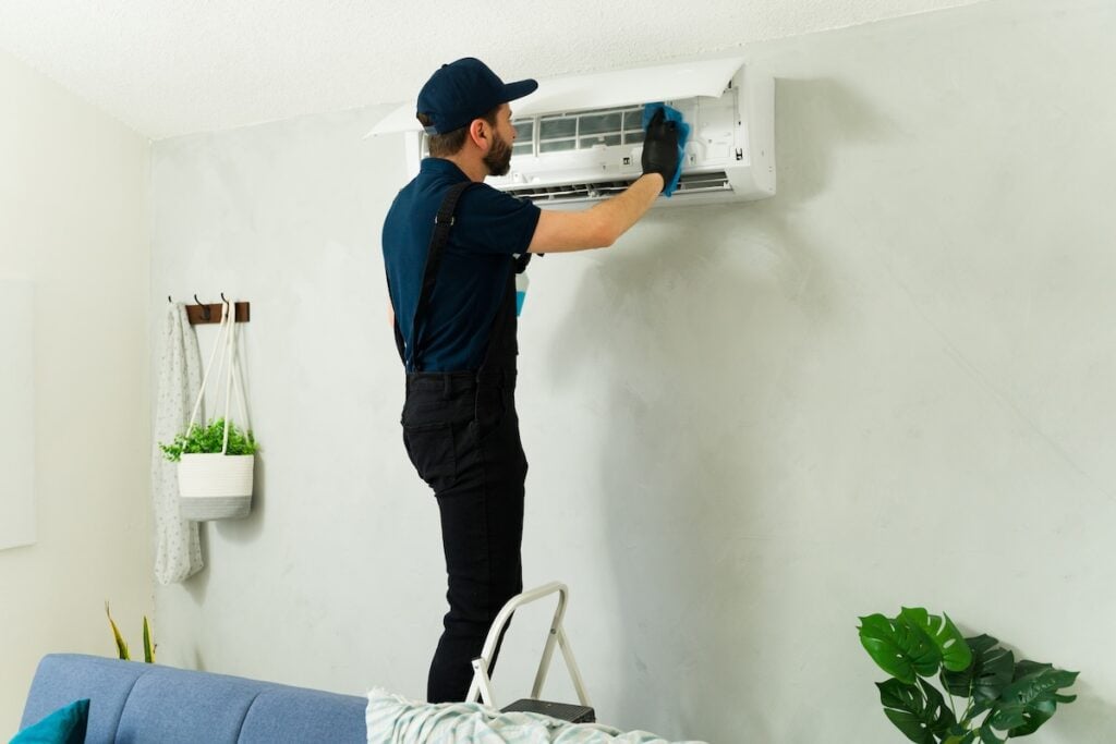 Technician performing maintenance on mini split air conditioning system, cleaning filters and vents with detergent and sponge