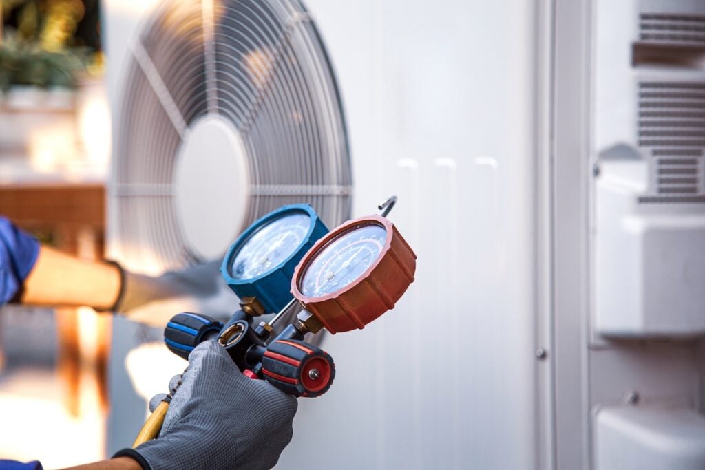Heat and Air Conditioning, HVAC system service technician using measuring manifold gauge checking refrigerant and filling industrial air conditioner after duct cleaning maintenance outdoor compressor.