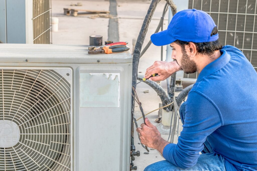 a professional electrician man is fixing a heavy duty unit of central air conditioning system by his tools on the roof top and wearing blue color of uniform and white cap ac not turning on
