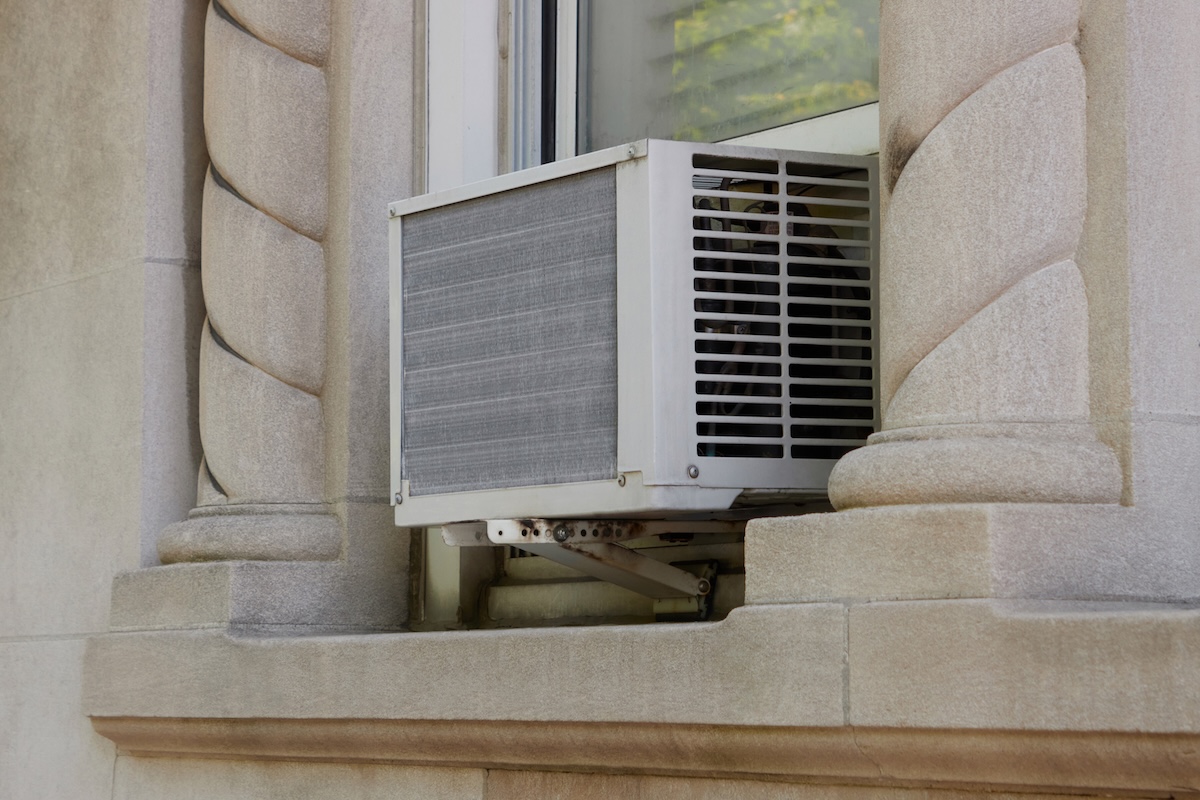 exterior view of air conditioning window unit extruding from the window sill with a portable safety ledge support installed under it, with elegant, decorative concrete architectural details