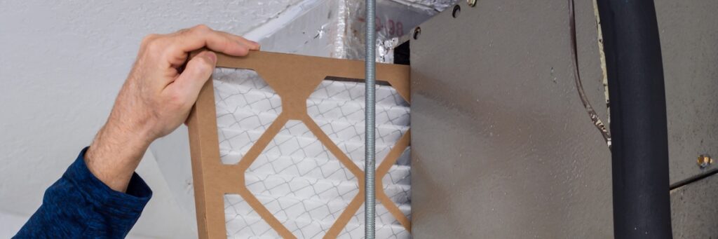 HVAC service technician changing dirty indoor air filter in residential heating and air conditioning system. Home air duct ventilation system maintenance for clean air.