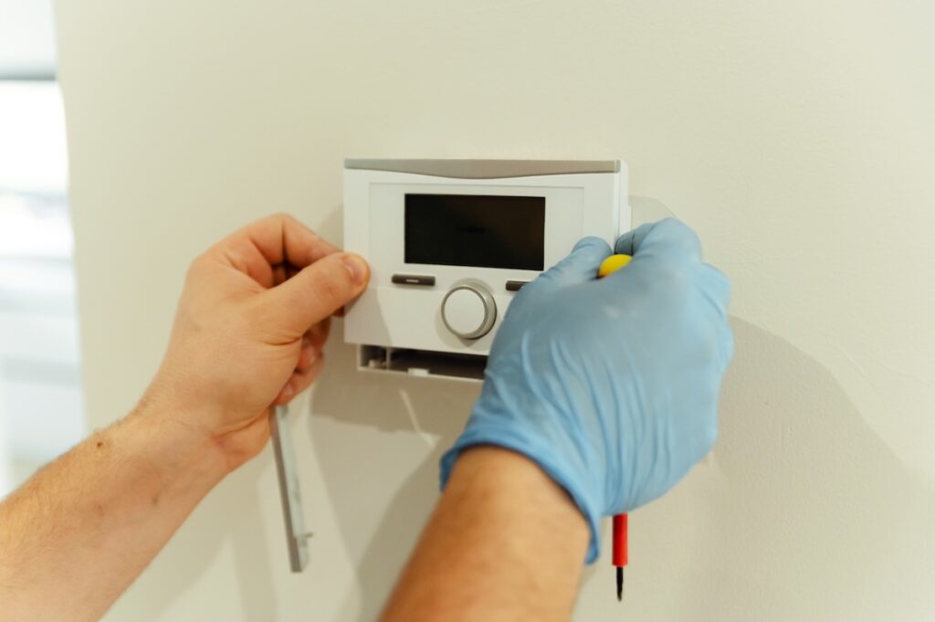 thermostat replacement electrician, male electrician repairs smart home with a screwdriver. electrical engineer installs and programs smart home.