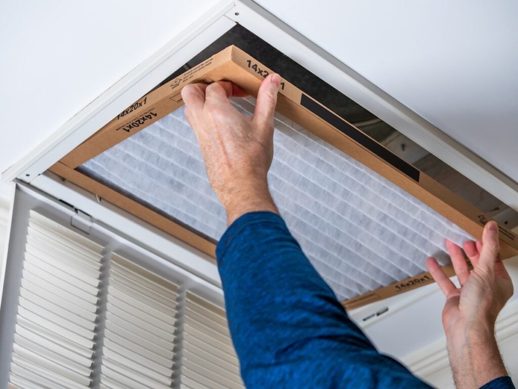 how to clean air ducts Man replacing dirty HVAC air filter in ceiling vent. Home air duct system maintenance for clean air.