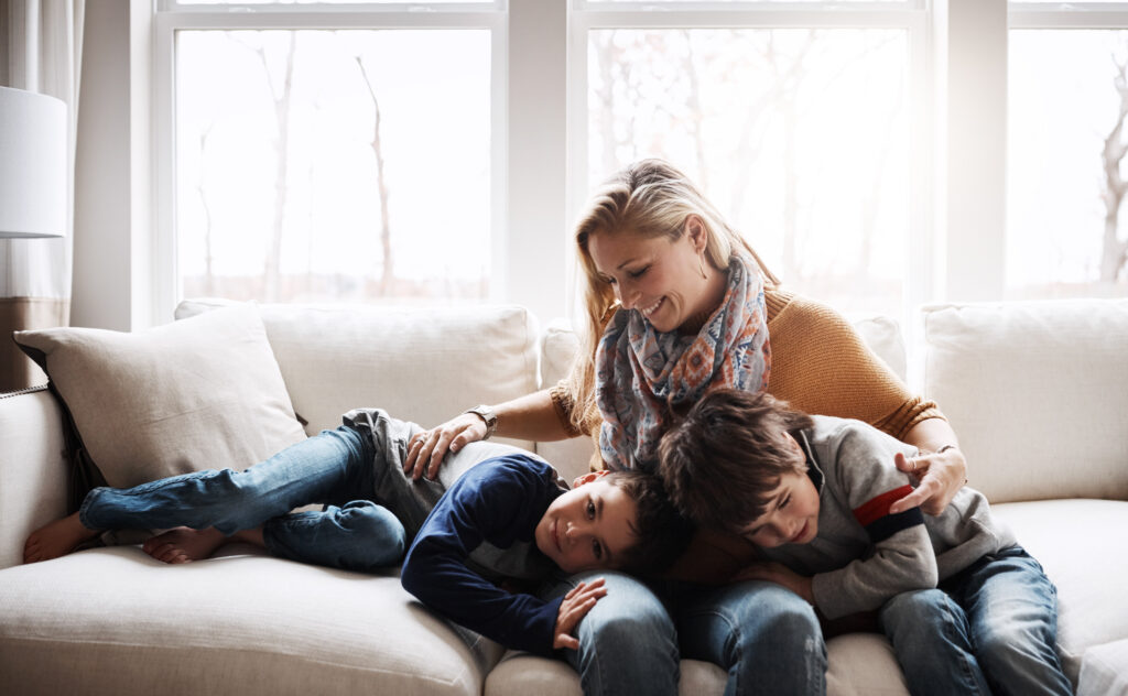 Happy family, mother bonding with children and relax on sofa for love, care and smile at home together. People, mom and kids lying on couch in the living room for cozy winter hug or fun with parent.