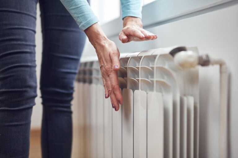 Woman heating her hands on the radiator during cold winter days.