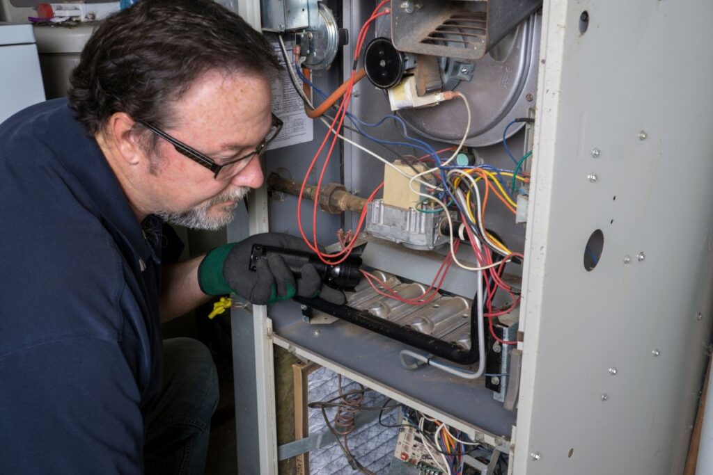 furnace keeps shutting off technician using flashlight to inspect wires